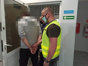 Policjanci z zatrzymanym mężczyzną przed pomieszczeniem dla osób zatrzymanych