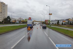 Miejsce wypadku z udziałem osób pieszych. Na jezdni radiowóz, samochody biorące udział w zdarzeniu. Znak z informacją o wypadku