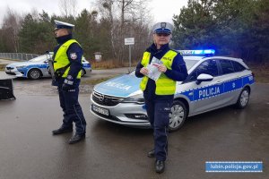 Policjanci stoją przy radiowozie, policjantka trzyma laurkę otrzymaną od dzieci