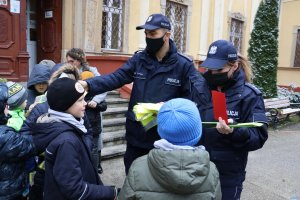 Policjant i policjantka rozdają dzieciom kamizelki odblaskowe