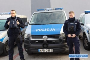 policjanci w umundurowaniu przed radiowozem oznakowanym typu bus