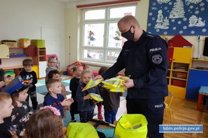 Policjant rozdaje kamizelki odblaskowe dzieciom