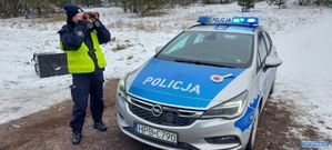 Policjantka przy radiowozie patrzy przez lornetkę