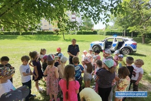 Policjantka w trakcie prelekcji z dziećmi na boisku. W tle radiowóz