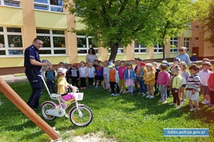 Policjant podczas prelekcji z dziećmi, dziewczynka na rowerze. Spotkanie z przedszkolakami