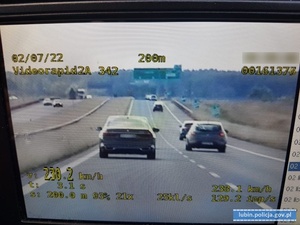 samochód osobowy koloru ciemnego na wyświetlaczu wideorejestratora. W dolnym lewym roku prędkość zmierzona 230 km/h