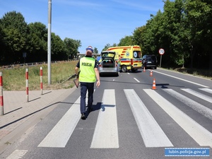 Policjant na miejscu wypadku drogowego idzie w kierunku pojazdu sprawcy i karetki pogotowia