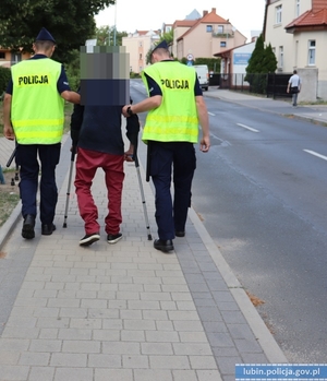 Policjanci prowadzą starszego mężczyznę idącego o kulach