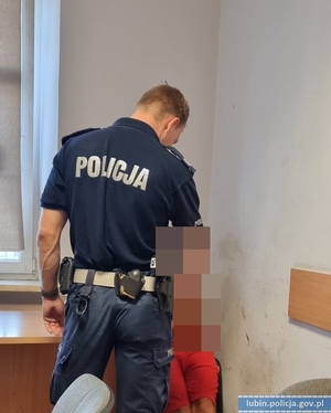 Policjant stoi przy zatrzymanym kierującym, który siedzi na krześle