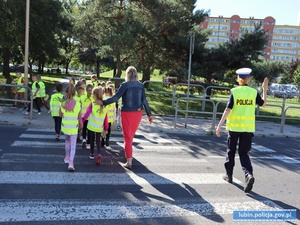 Policjantka wstrzymuje ruch, dzieci przechodzą przez przejście dla pieszych