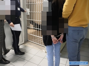 Policjanci z zatrzymaną kobietą przed pomieszczeniem dla osób zatrzymanych