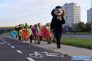 Dzieci z transparentami i komisarzem lwem idą chodnikiem