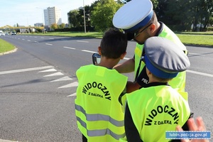 Policjant ruchu drogowego pokazuje dzieciom jak mierzy się prędkość kierującym za pomocą ręcznego pomiaru prędkości