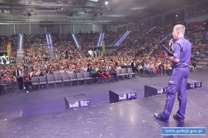 Policjant stoi na scenie przed publicznością, omawiając metody oszustw