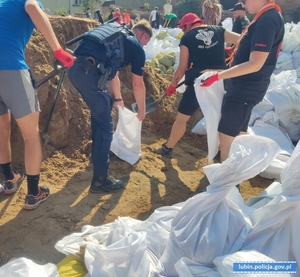 Policjanci pomagają przy pakowaniu worków z piaskiem