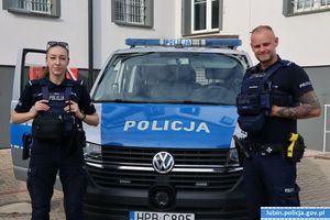 Policjantka i policjant stoją przed radiowozem