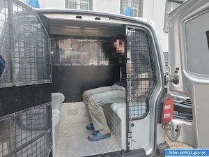 otwarte drzwi radiowozu w środku siedzi mężczyzna z rękoma trzymanymi z tyłu.