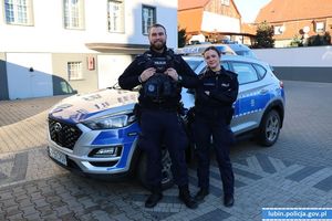 Policjantka i policjant stoją przy radiowozie