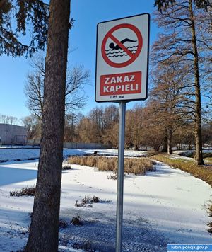 na zdjęciu widać zamarznięty staw pokryty śniegiem i znak zakaz kąpieli