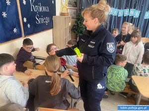 Policjantka rozdaje uczniom odblaski