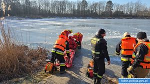 ćwiczenia na zamarzniętym zbiorniku wodnym  policjanci i strażacy przyglądający się czynnościom ratowniczym prowadzonym na zamarzniętej tafli lodu