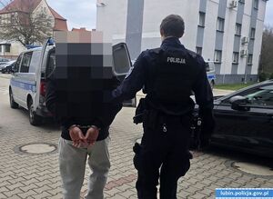 Policjant prowadzi zatrzymanego do radiowozu