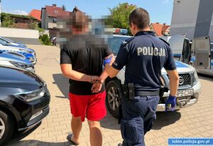 Policjant prowadzi zatrzymanego mężczyznę do radiowozu