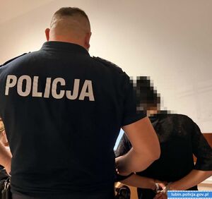 Kobieta z kajdankami na rękach stoi z policjantem
