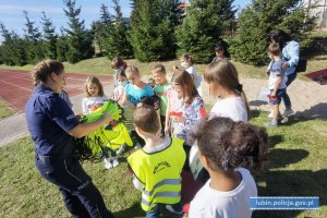 Policjantka rozdaje grupie dzieci worki odblaskowe