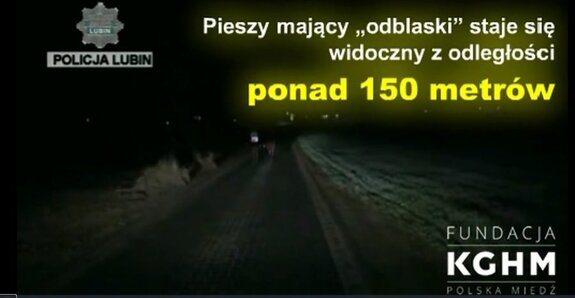 Dwie osoby o zmierzchu idą ulicą, Osoba po lewej stronie ma ubraną kamizelkę. Osoba po prawej stronie jest ubrana w ciemną odzież. Kadr ze spotu