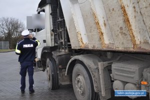 Policjant stoi przy samochodzie ciężarowym. Rozmawia z kierującym, który siedzi w kabinie