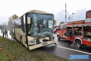 Miejsce zdarzenia drogowego. Autobus z rozbitą przednią szybą, strażacy i policjanci w tle