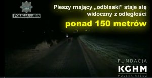 Dwie osoby idą drogą. Jedna nie ma kamizelki, a druga ma na sobie kamizelkę odblaskową. Po prawej stronie zdjęcia jest napis: Pieszy mający odblaski staje się widoczny z odległości ponad 150 metrów