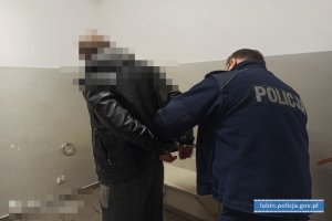 Policjant zakłada mężczyźnie kajdanki na ręce trzymane z tyłu