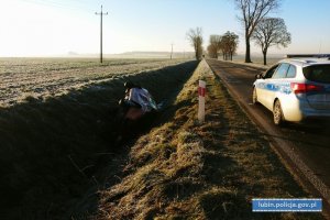 Samochód leży w rowie. Na drodze stoi radiowóz