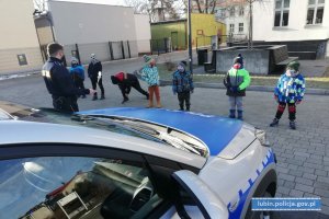 Policjant prowadzi prelekcje dla dzieci. W tle radiowóz