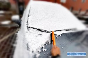 ręka mężczyzny ze zmiotką odśnieżająca maskę samochodu osobowego