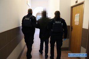 Policjanci prowadzą podejrzanego, który ma założone kajdanki zespolone