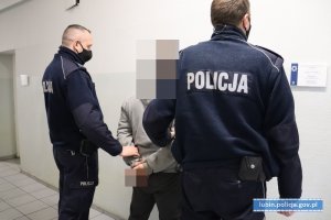 Policjanci stoją z zatrzymanym mężczyzną, który ma na rękach kajdanki