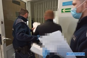 Policjanci prowadzą zatrzymanego do pomieszczenia dla osób zatrzymanych