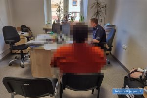 Policjant przy biurku przesłuchuje osobę zatrzymaną siedzącą na krześle