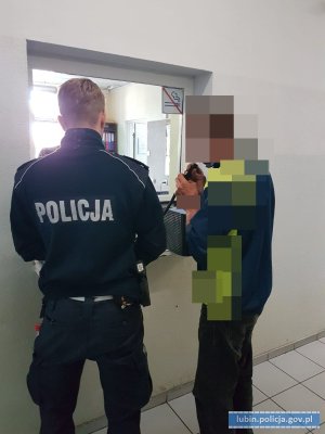 Mężczyzna dmucha w alkomat. Obok stoi policjant