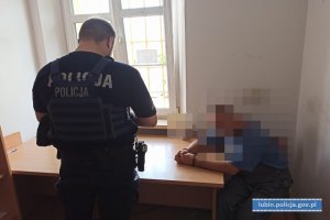 Policjant z zatrzymanym nietrzeźwym kierującym w pomieszczeniu. zatrzymany siedzi, policjant stoi