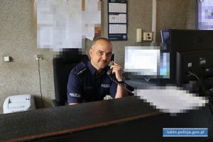 Policjant dyżurny przy biurku rozmawia przez telefon