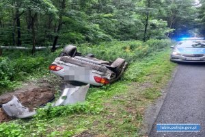 Auto przewrócone da dach leży w rowie. W tle radiowóz policji