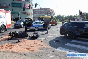 Miejsce zdarzenia drogowego. Na miejscu leżący motocykl, straż pożarna, policja, karetka pogotowia