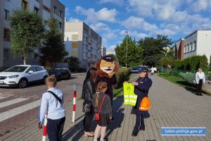 Policjantka przed szkołą wraz z komisarzem Lwem przed szkołą rozdaje kamizelki odblaskowe dzieciom